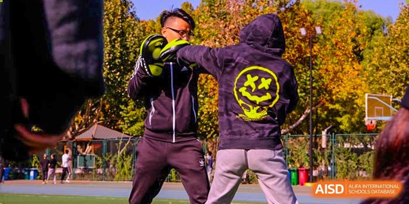 Two students practice boxing drills outdoors, with one wearing a hoodie and the other holding focus mitts to improve striking accuracy at Beijing Tongzhou Shuren Private School.
