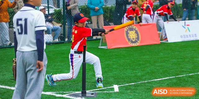 A student athlete in a red jersey focuses on hitting a baseball off a tee during a structured outdoor physical education lesson on the green turf at Beijing Tongzhou Shuren Private School.
