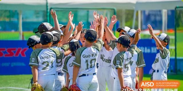 A youth baseball team huddles together with their hands raised in a high-five gesture to celebrate a successful play on the outdoor sports field at Beijing Tongzhou Shuren Private School.