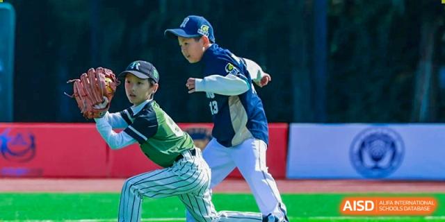 Two baseball players in green and blue uniforms compete for the ball during an active and energetic afternoon match on the school's sports diamond at Beijing Tongzhou Shuren Private School.