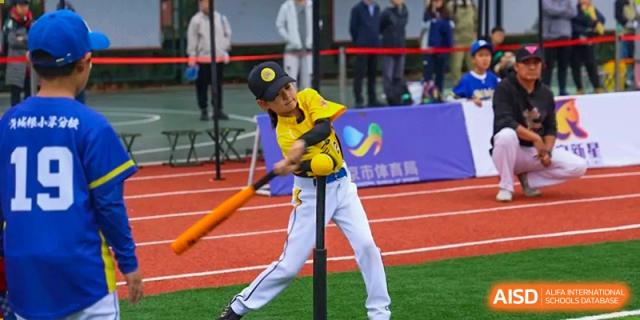 A student in a yellow and black uniform takes a powerful swing at a ball during a baseball game, demonstrating athletic skill and coordination at Beijing Tongzhou Shuren Private School.