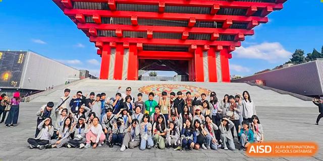 A massive group of students and teachers pose for a commemorative photo in front of a giant traditional red architectural gate during a cultural field trip for the Korean International School In Beijing.