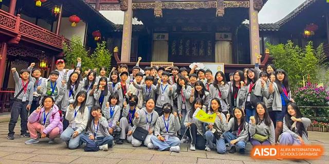 Students smile and cheer while gathered in front of a historic temple building to capture a joyful memory during an educational cultural excursion with the Korean International School In Beijing.