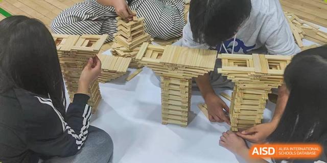 Two students focus intently on building complex pillars and bridge structures using hundreds of thin wooden slats during a hands-on engineering workshop at the Korean International School In Beijing.