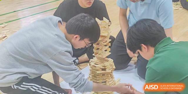 A young man carefully adds a wooden slat to a very tall and narrow tower, showing great concentration during a creative construction competition held at the Korean International School In Beijing.