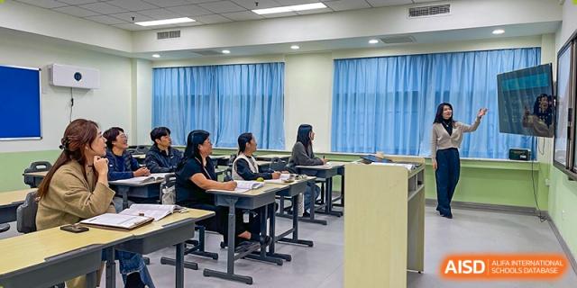 A group of parents or teachers sits in rows of desks while listening to a presentation from a speaker at the front of a modern classroom at the Korean International School In Beijing.