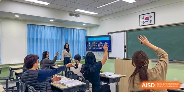 An instructor stands by a large digital screen while a student in the classroom raises their hand to ask a question during an informative session at the Korean International School In Beijing.