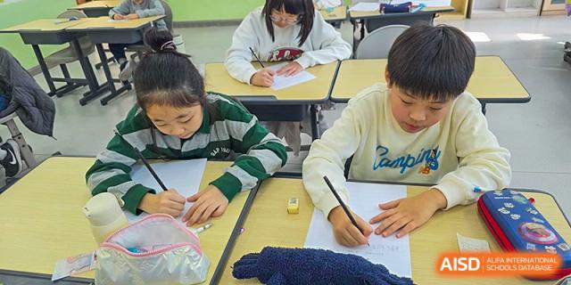 Two students sit side-by-side at their desks, diligently working on their individual writing assignments in a quiet classroom at the Korean International School In Beijing.