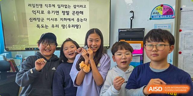 A group of four students pose closely together, smiling and laughing while showing off small items during a break between classes at the Korean International School In Beijing.