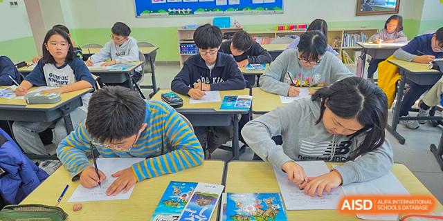 Students are seen from a high angle as they work collaboratively and individually on their colorful workbooks during a busy class at the Korean International School In Beijing.