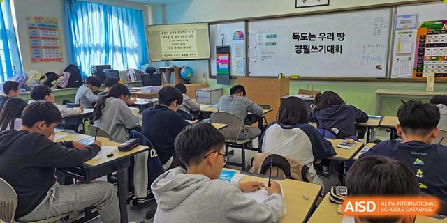 Students sit at their desks in a classroom, focused on a writing competition about Dokdo being displayed on the front whiteboard at the Korean International School In Beijing.