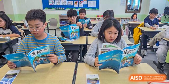 A group of students sit together reading educational booklets with blue covers, focusing on a lesson about maritime geography at the Korean International School In Beijing.