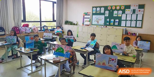 Young elementary students sit at their desks holding up colorful drawings and posters they created during an art and geography lesson at the Korean International School In Beijing.