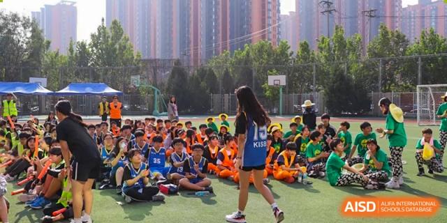 A large group of students in colorful athletic uniforms sit and stand on an outdoor basketball court during a school-wide assembly at the Korean International School In Beijing.