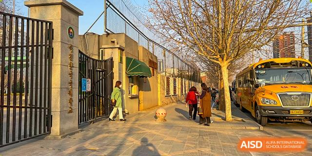 People walk along the sidewalk outside the gated entrance and brick perimeter wall of the campus during a sunny afternoon at the Korean International School In Beijing.