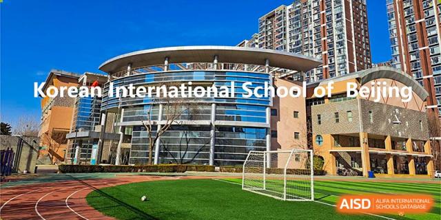 The bright green turf of the school soccer field sits in front of a unique circular glass building under a clear blue sky at the Korean International School In Beijing.