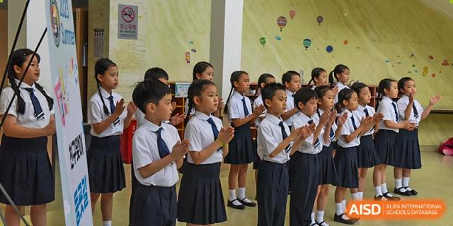 A group of young students in formal white shirts and navy ties stand in a row and politely clap their hands during a school performance or assembly held at the Korean International School In Beijing.