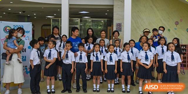 Students in matching uniforms stand together in a bright, modern lobby area while being supervised by staff members during an event at the Korean International School In Beijing.