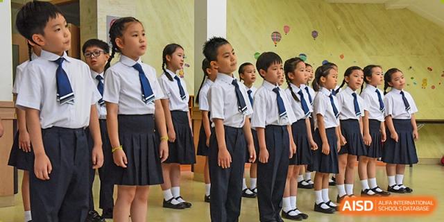 Rows of elementary students stand at attention with respectful expressions while participating in a formal ceremony or singing the anthem at the Korean International School In Beijing.