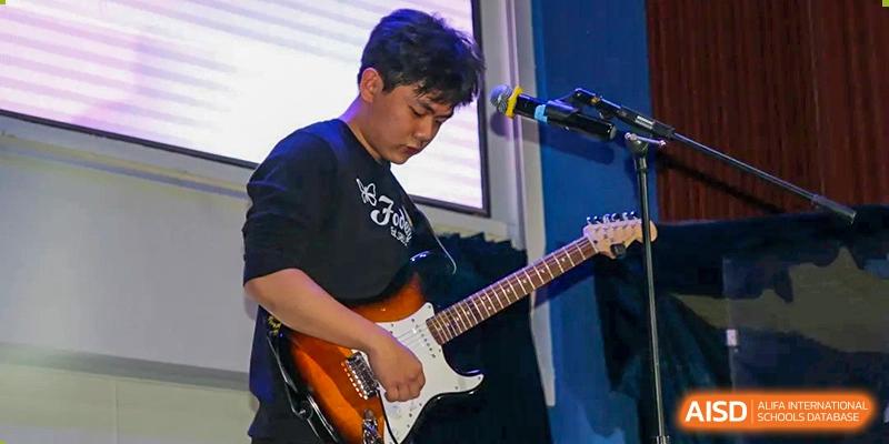 A close-up of a student focused on playing an electric guitar during a live musical performance on stage at Korean International School In Beijing.