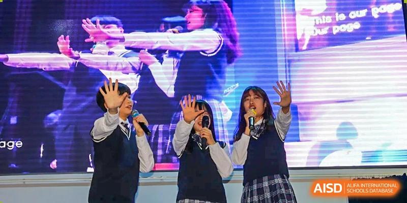 Three students singing and gesturing toward the audience during a stage performance at Korean International School In Beijing.