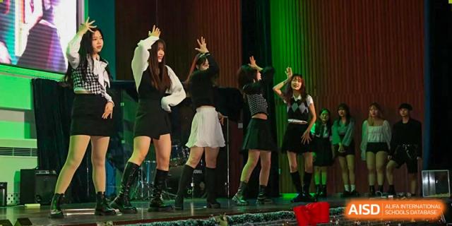 A group of students performs a modern dance routine under green stage lighting at Korean International School In Beijing.