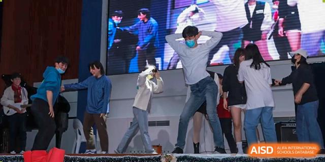Students perform a high-energy dance routine in front of a large video screen at Korean International School In Beijing.
