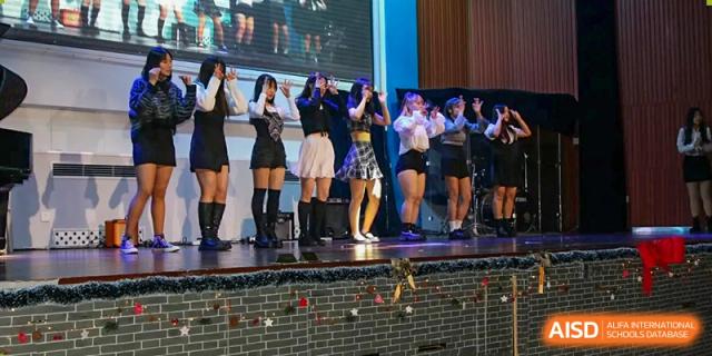 A group of students in dark outfits perform a synchronized dance routine on a decorated stage at Korean International School In Beijing.