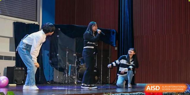 A student singer performs on stage while others kneel beside her during a theatrical piece at Korean International School In Beijing.