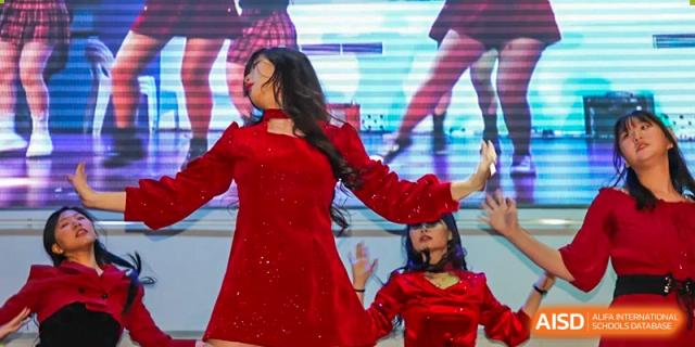 A student in a sparkling red dress performs a dance solo on stage in front of a digital screen at Korean International School In Beijing.