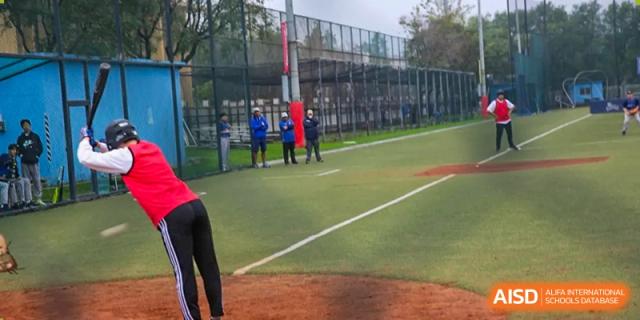 A wide shot of a baseball game in progress on an outdoor field with players positioned across the diamond at Korean International School In Beijing.