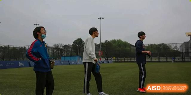 Three baseball players stand together on the outfield grass during a team practice session at Korean International School In Beijing.