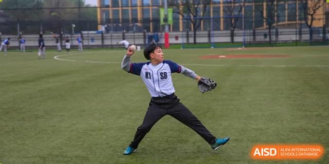 A pitcher in a white and navy "KISB" jersey winds up to throw a ball during a baseball match at Korean International School In Beijing.