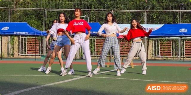 A group of four female students performs an energetic synchronized dance routine in stylish casual wear on an outdoor court at the Korean International School In Beijing.