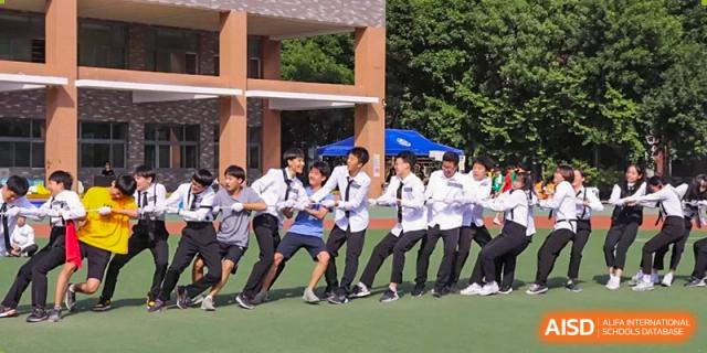 A team of students in blue and white baseball uniforms and matching caps poses together for a team photo in front of a green fence at the Korean International School In Beijing.