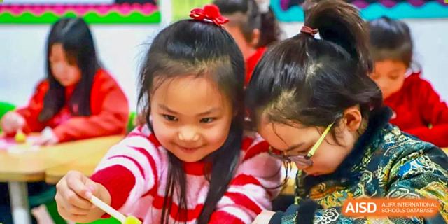 A young girl with glasses and a red-and-white striped sweater works intently on a hands-on creative project during a classroom activity at Beijing World Youth Academy.
