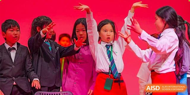 Students perform an expressive choreographed dance routine on a bright pink stage, wearing formal school uniforms during a creative arts showcase event at Beijing World Youth Academy.