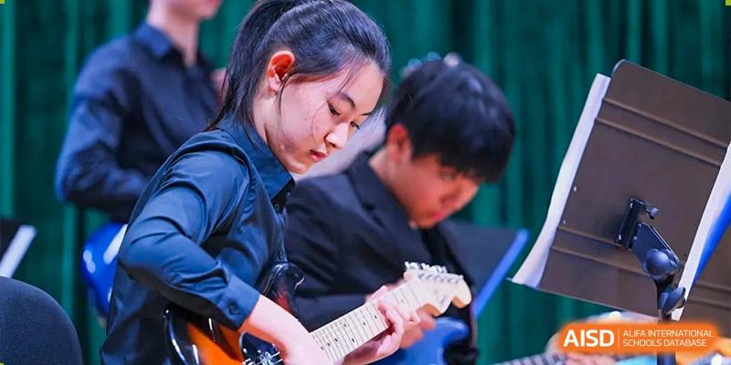 A student focused on playing an electric guitar during a live musical performance or rehearsal with the school ensemble at Beijing World Youth Academy.