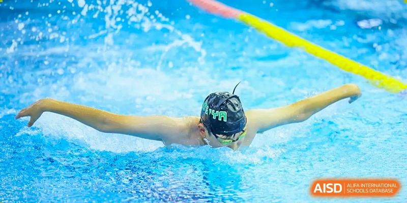 A student athlete wearing a swim cap and goggles performs the butterfly stroke during a competitive swimming event hosted by Beijing World Youth Academy.