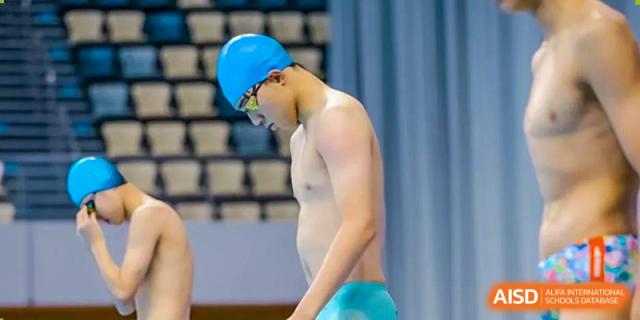 A male swimmer in a blue cap stands at the edge of the pool, preparing for his heat during a competitive swim meet at Beijing World Youth Academy.