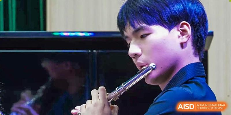 A close-up of a student musician focused on playing the flute during a concert performance at Beijing World Youth Academy.