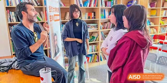 Two students discuss a project while standing in a library filled with books and learning resources at Griffin International Academy.