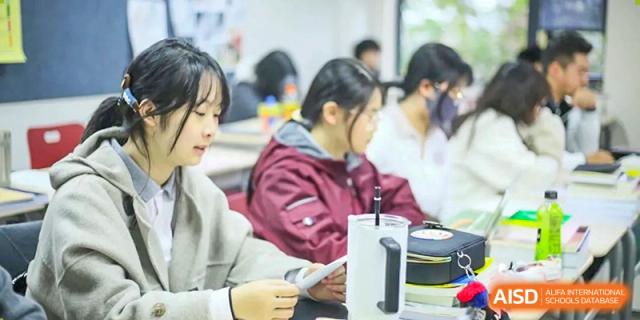 A female student in a maroon jacket focuses on her notes during a collaborative class session at Griffin International Academy.