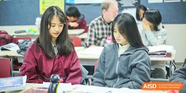 Two female students share a joyful moment while working together on a laptop in a bright and modern classroom at Griffin International Academy.