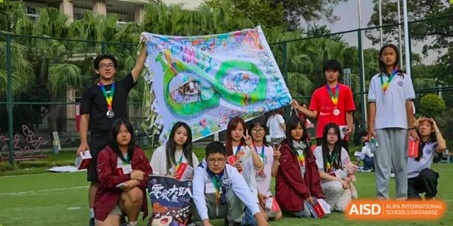 Students in red and white athletic wear gather together to display a colorful handmade banner during a sports event at Griffin International Academy.