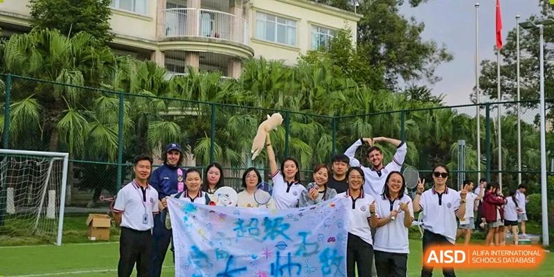 A group of staff and students hold up a large banner while posing for a commemorative photo on an outdoor field at Griffin International Academy.