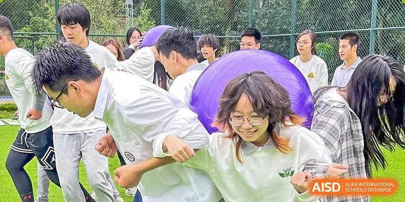 Students in white shirts work together and laugh while participating in a collaborative team-building activity outdoors at Griffin International Academy.