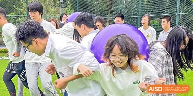 Students in white shirts work together and laugh while participating in a collaborative team-building activity outdoors at Griffin International Academy.