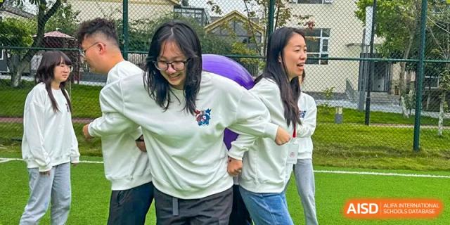 Two female students smile while participating in a collaborative team-building race with a large exercise ball at Griffin International Academy.