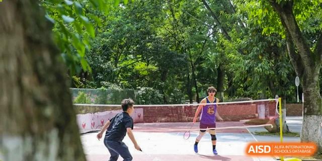 Two students compete in an outdoor badminton or tennis match on a paved court surrounded by trees at Griffin International Academy.